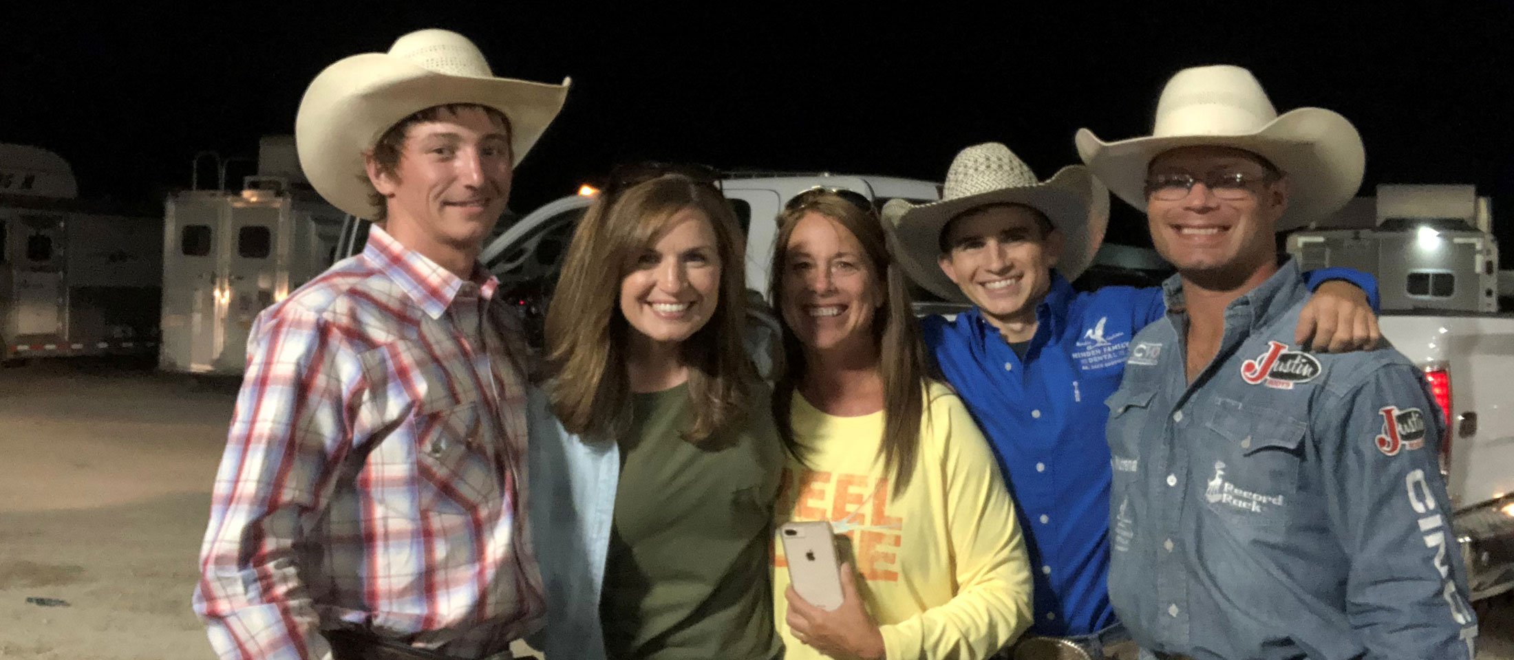 A group of men and women hugging in front of trucks and trailers.